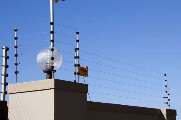 Electric fence wires and rod at the top of the wall with sky blue background